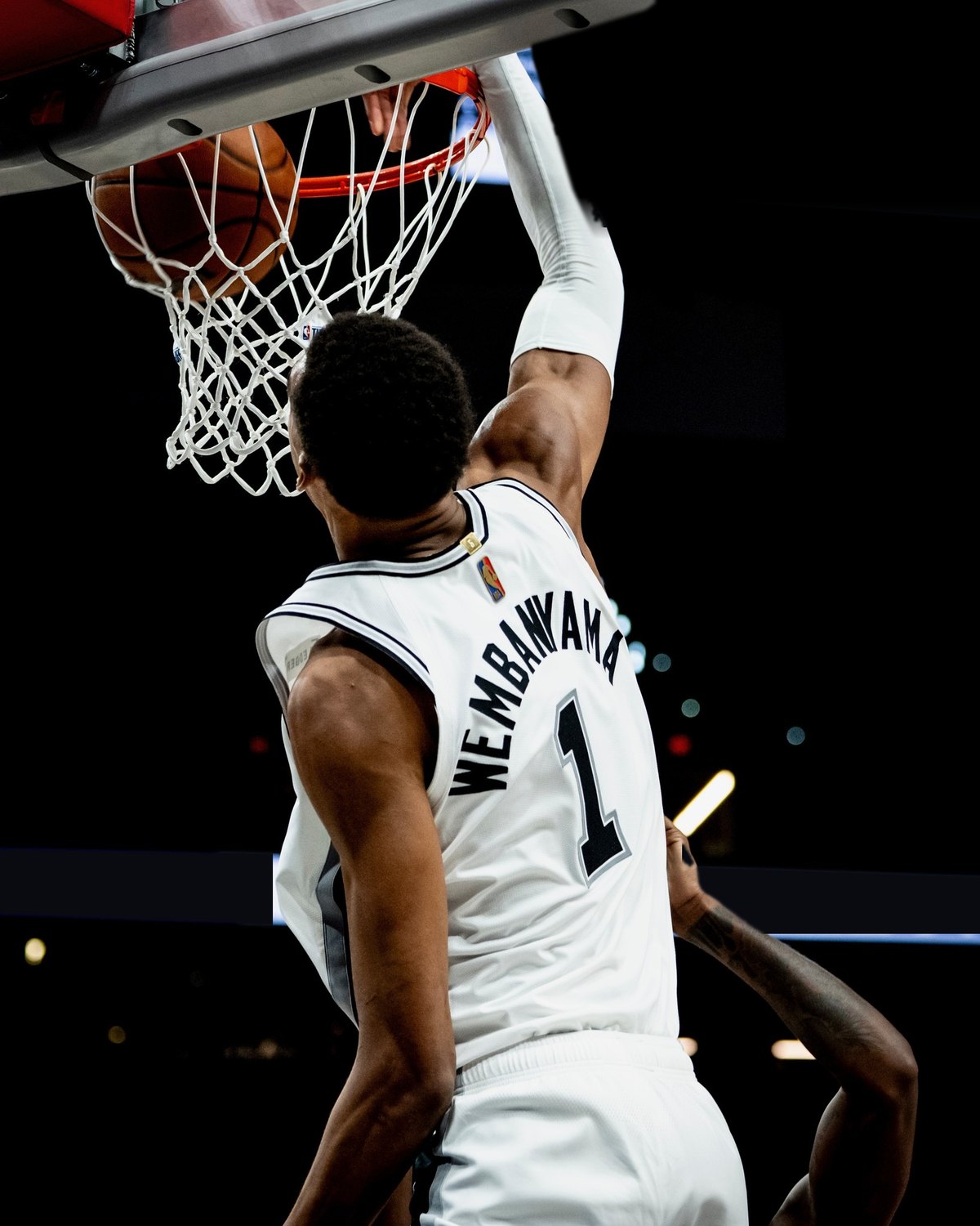 Victor Wembanyama de dos, accroché au cercle après un dunk